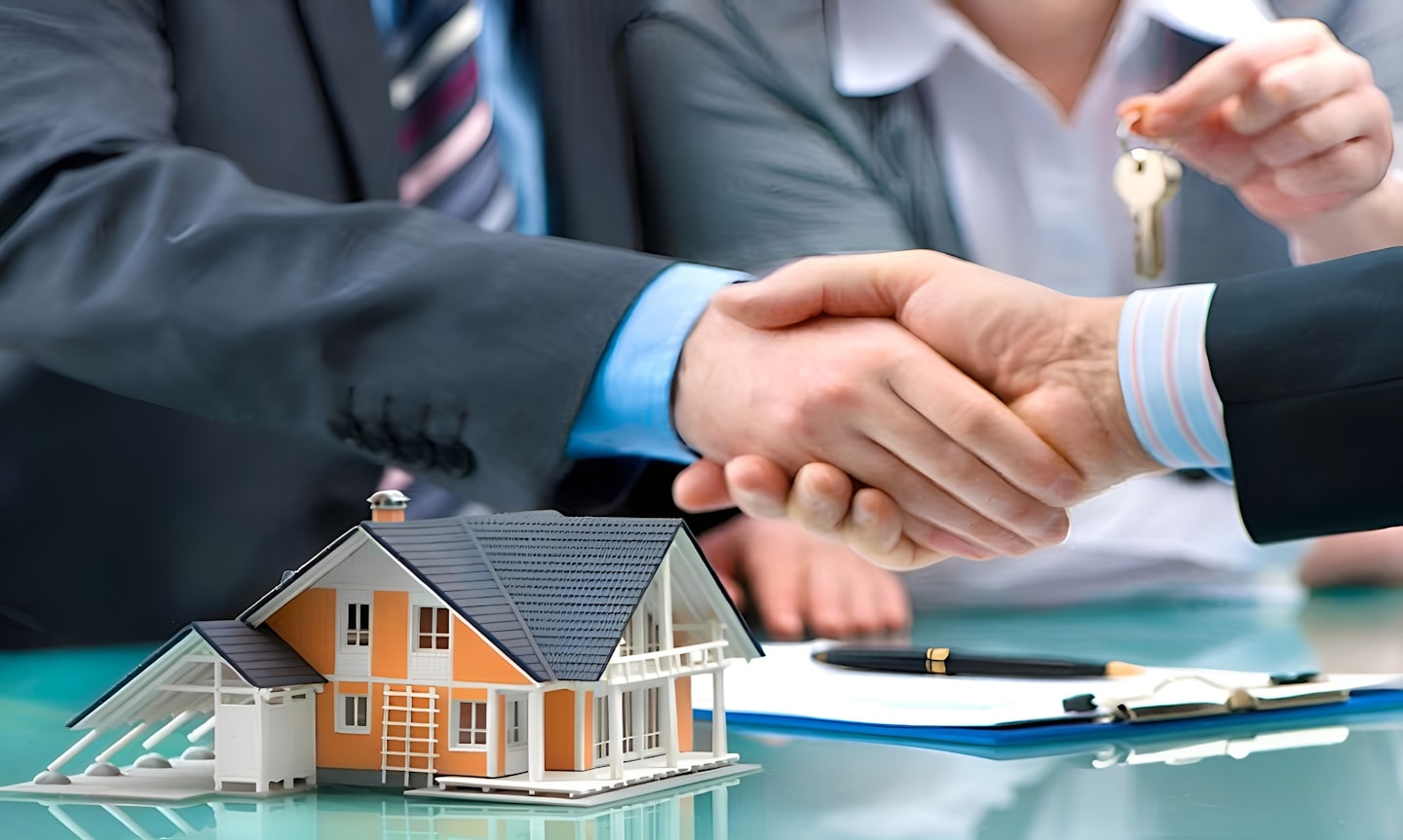 Business people shaking hands over a table with house model.