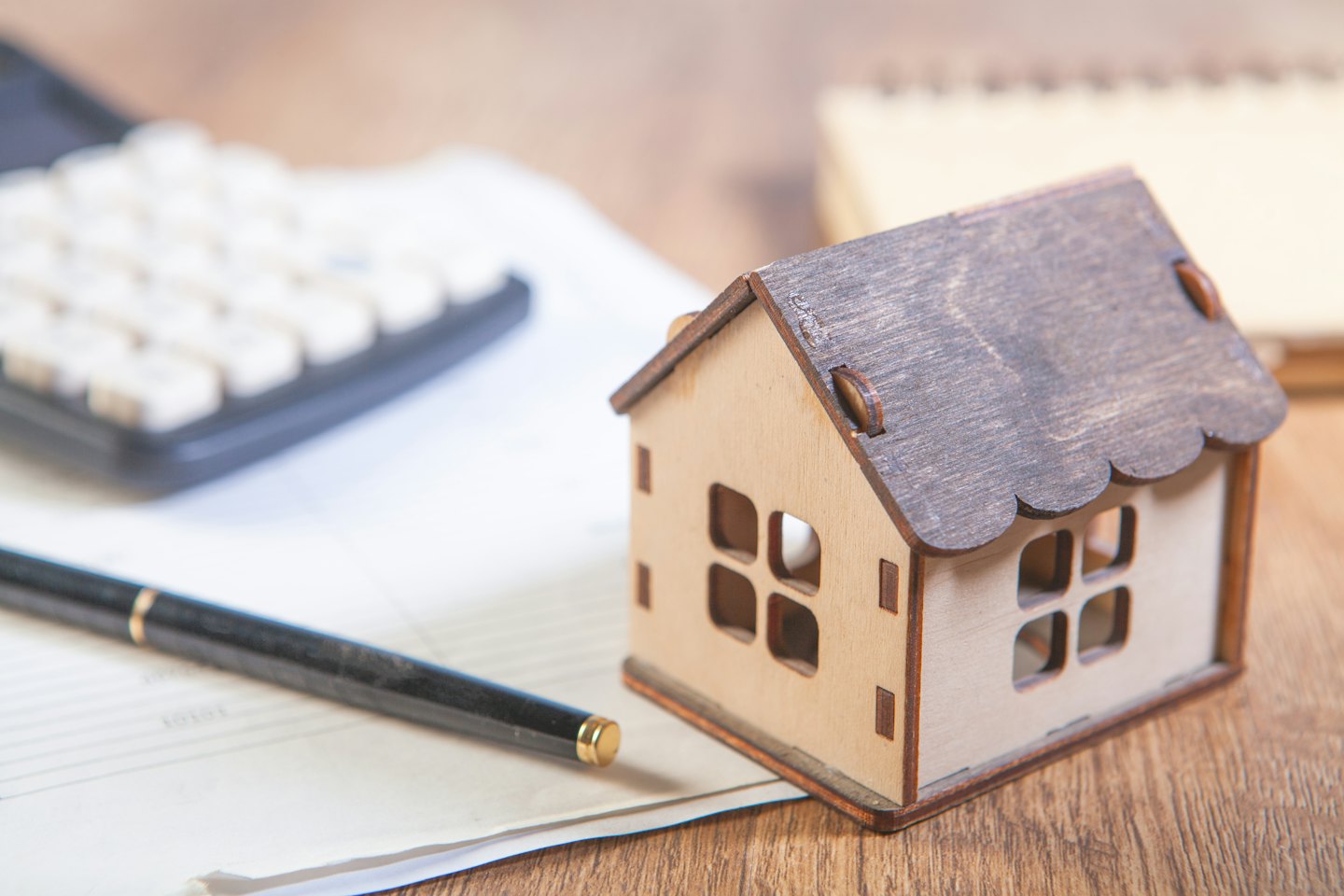 Small wooden model house on a wooden desk with office supplies.